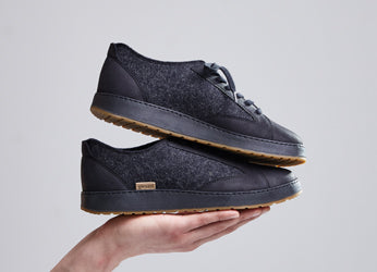 A picture of two Charcoal grey colored Langdal sneakers are displayed stacked on an outstretched hand
