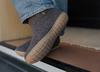 A close-up picture of a pair of glerups boots in the color Chestnut brown worn by a person standing in a doorway.