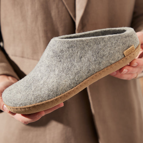 Close-up picture of hands holding a Grey glerups slip-on with a leather sole.