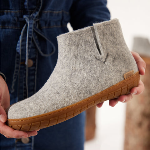 Close-up picture of hands holding a Grey glerups boot with a natural rubber sole.