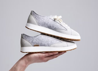 Two glerups Langdal sneakers in the color Grey are balanced on an outstretched hand, with the shoes stacked on each other.