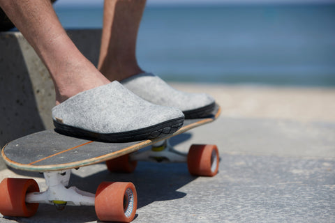 A person is standing on a skateboard wearing Grey glerups slip-ons with black rubber soles.